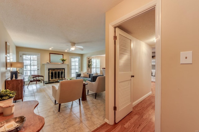 living room featuring a wealth of natural light, a glass covered fireplace, ceiling fan, and a textured ceiling