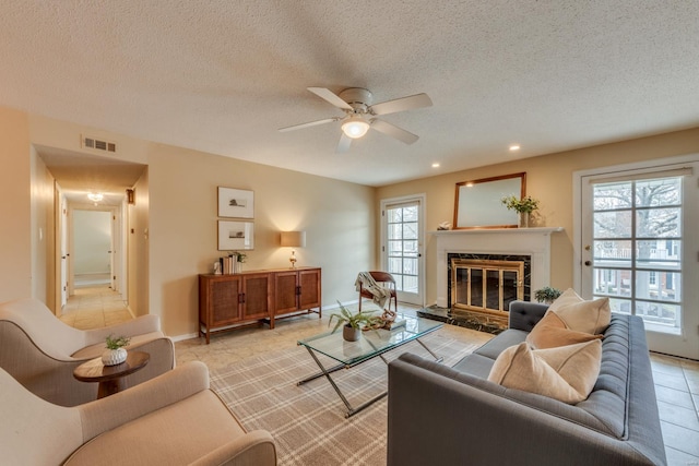 living area with light tile patterned floors, visible vents, a ceiling fan, a glass covered fireplace, and a textured ceiling