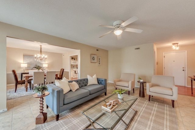 living room featuring a textured ceiling, light tile patterned flooring, ceiling fan with notable chandelier, and visible vents