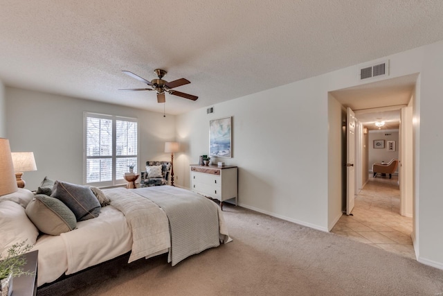 bedroom with baseboards, visible vents, a ceiling fan, light colored carpet, and a textured ceiling