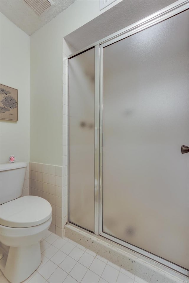 bathroom with tile walls, visible vents, toilet, a stall shower, and tile patterned flooring