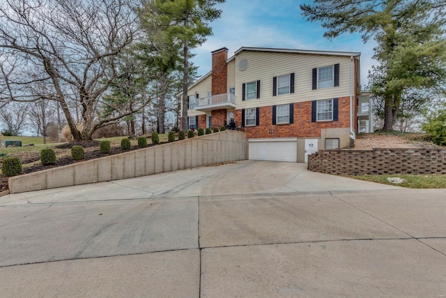 view of side of home with a garage, brick siding, driveway, and a chimney