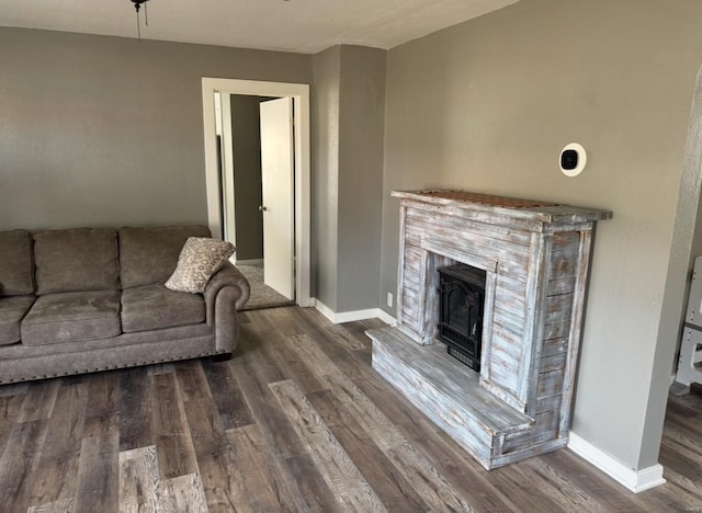 living area featuring a fireplace with raised hearth, baseboards, and wood finished floors