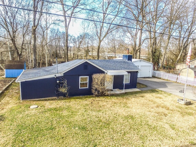 view of front facade with an outbuilding, fence, roof with shingles, a front yard, and a garage