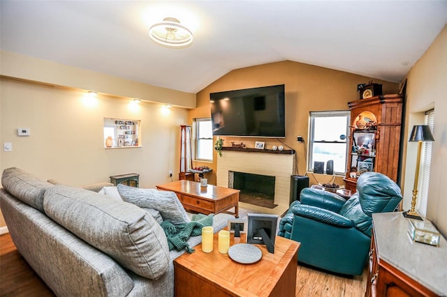 living area featuring vaulted ceiling, light wood-style flooring, and a fireplace