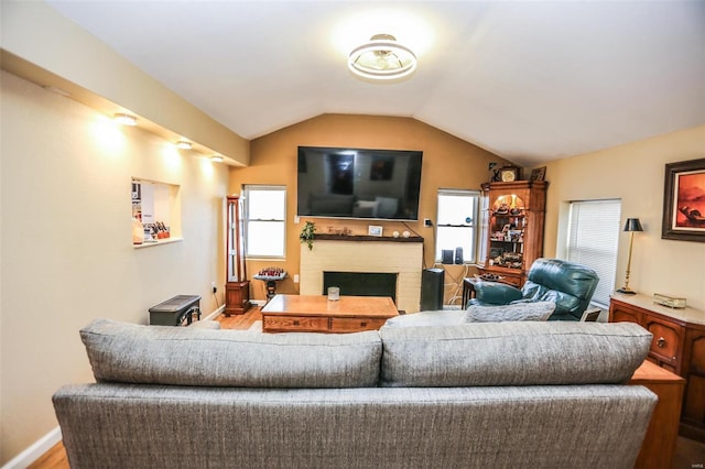 living area featuring baseboards, a brick fireplace, wood finished floors, and vaulted ceiling