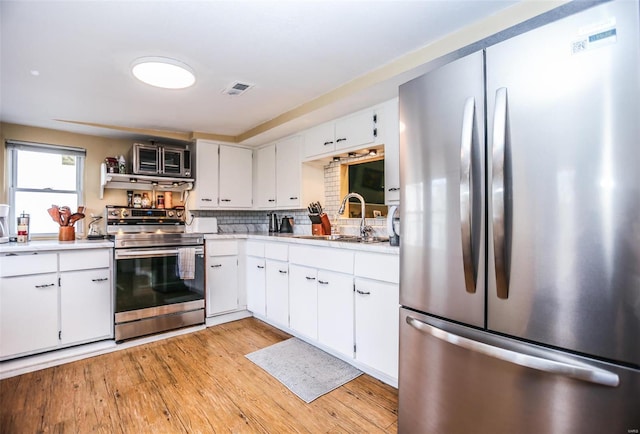 kitchen featuring light wood finished floors, a sink, stainless steel appliances, light countertops, and tasteful backsplash