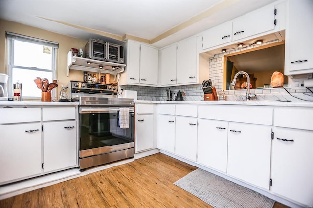 kitchen with backsplash, light countertops, light wood-style flooring, stainless steel electric range, and white cabinets