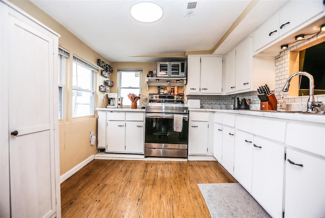 kitchen with light countertops, light wood-type flooring, backsplash, and stainless steel range with electric cooktop