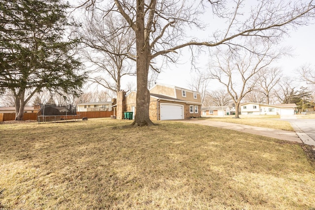 view of yard featuring a garage, a trampoline, concrete driveway, and fence