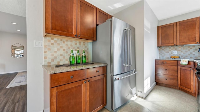 kitchen with tasteful backsplash, high quality fridge, light stone counters, and baseboards