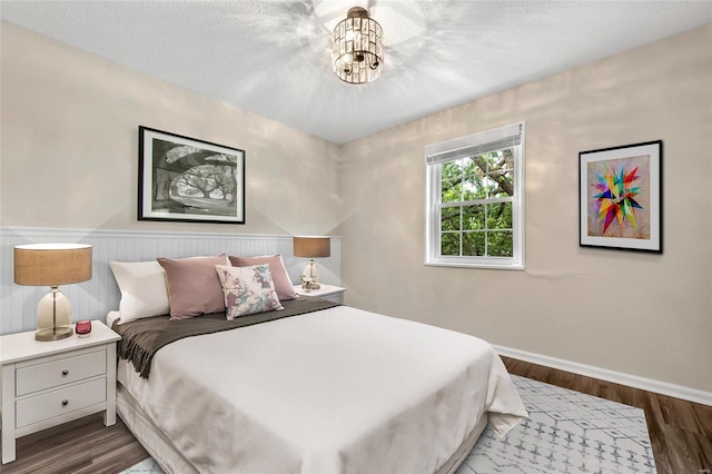 bedroom featuring a textured ceiling, a chandelier, dark wood finished floors, and baseboards