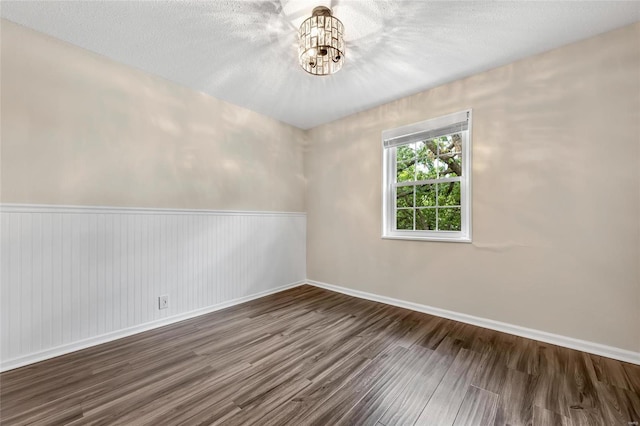 unfurnished room featuring a textured ceiling, a chandelier, wood finished floors, and wainscoting