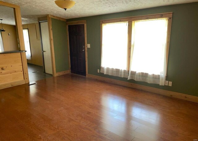 unfurnished room featuring a textured ceiling, baseboards, and wood finished floors