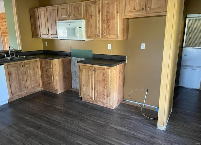 kitchen featuring dark countertops, dark wood finished floors, a sink, and white microwave