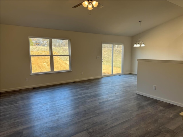 spare room featuring lofted ceiling, ceiling fan with notable chandelier, visible vents, baseboards, and dark wood finished floors