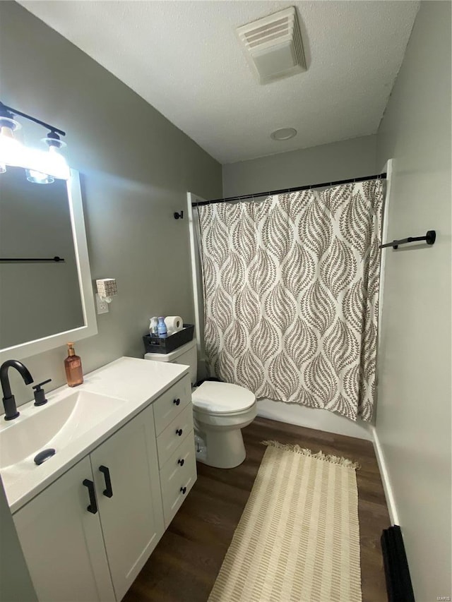 bathroom with visible vents, toilet, a textured ceiling, wood finished floors, and vanity