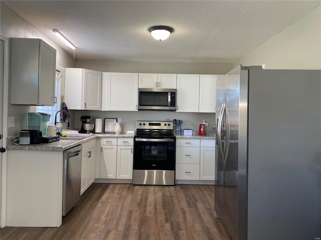 kitchen with a sink, a textured ceiling, white cabinetry, appliances with stainless steel finishes, and dark wood-style flooring