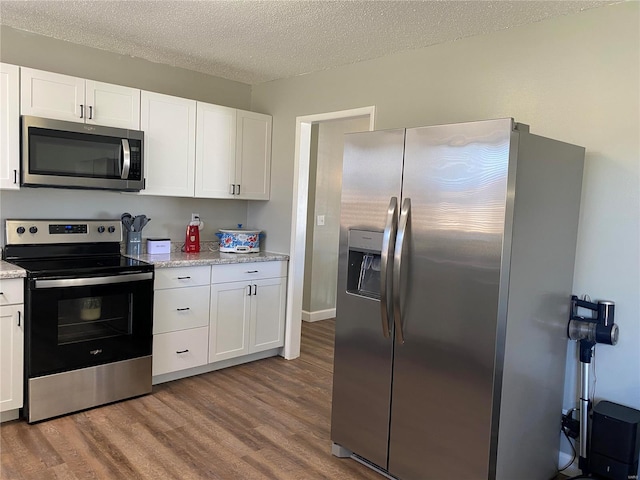 kitchen with white cabinetry, stainless steel appliances, a textured ceiling, and wood finished floors