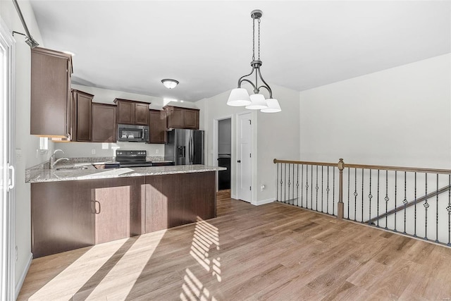 kitchen with dark brown cabinetry, light stone countertops, stainless steel appliances, light wood-style floors, and a sink