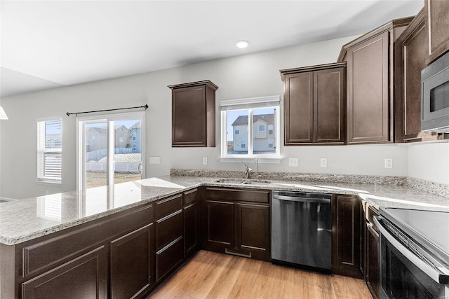 kitchen with light wood-style flooring, appliances with stainless steel finishes, a peninsula, dark brown cabinets, and a sink