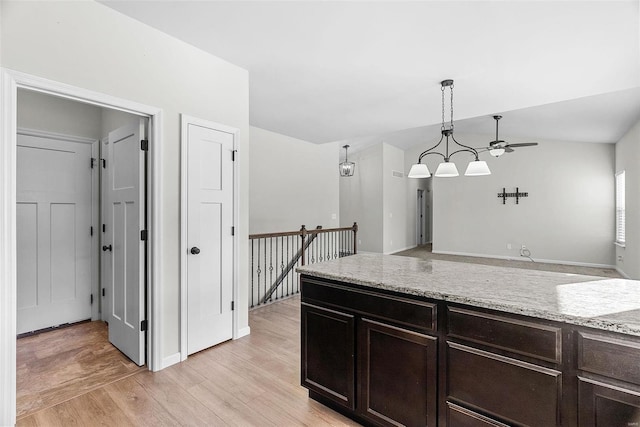 kitchen with dark brown cabinetry, light wood finished floors, light stone counters, vaulted ceiling, and pendant lighting