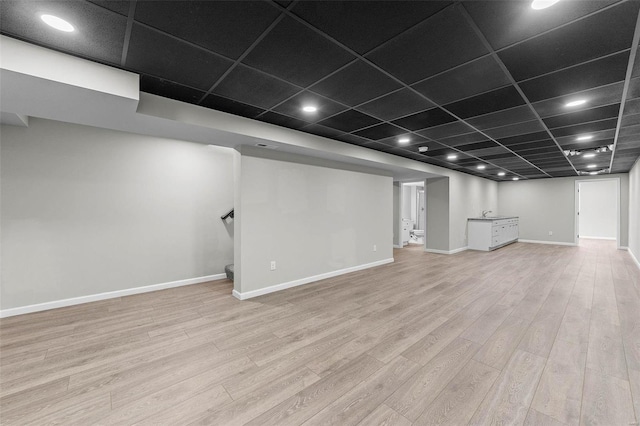 finished below grade area featuring a paneled ceiling, stairway, baseboards, and wood finished floors