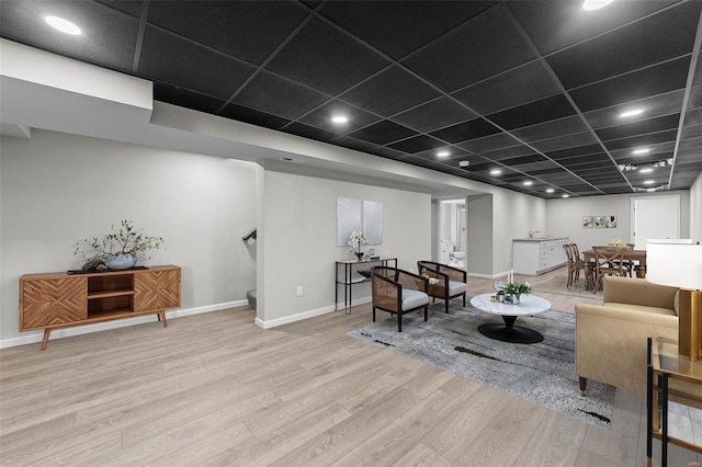 living area featuring a paneled ceiling, baseboards, and wood finished floors