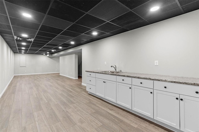 finished below grade area featuring light wood-style floors, a drop ceiling, a sink, and baseboards