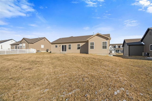 rear view of house with central air condition unit, a residential view, fence, and a lawn