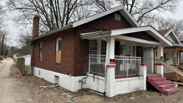 view of front of house with a porch, brick siding, and a chimney