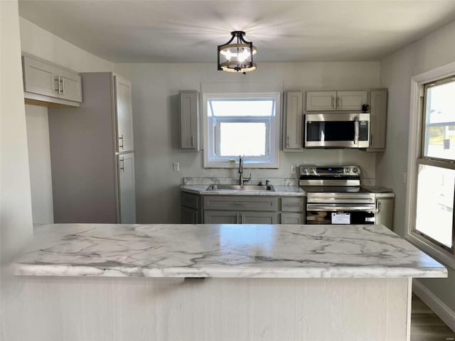 kitchen featuring gray cabinetry, baseboards, light stone countertops, stainless steel appliances, and a sink