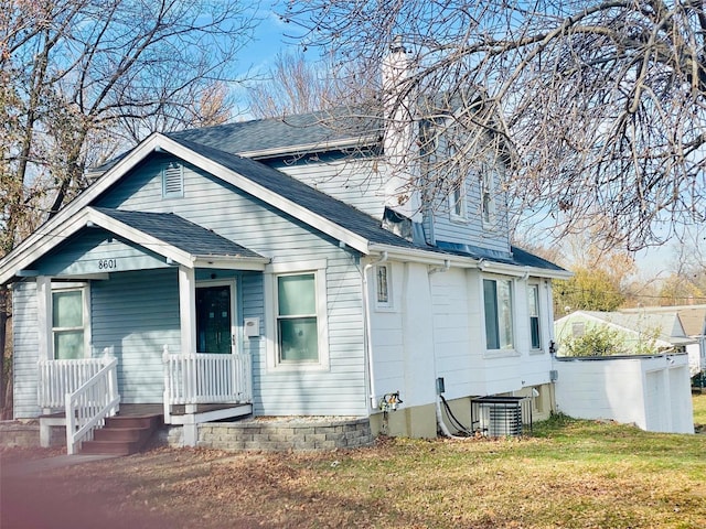 view of front of property with cooling unit, a chimney, a front yard, and a shingled roof