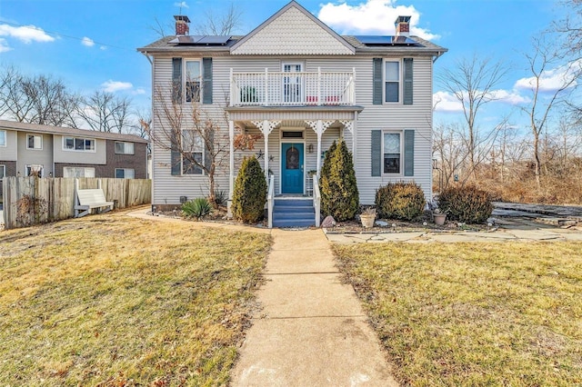 view of front of home featuring a front lawn, fence, a balcony, and roof mounted solar panels