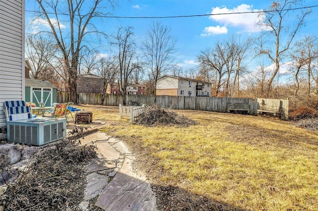 view of yard with an outbuilding, central air condition unit, a fire pit, fence, and a shed