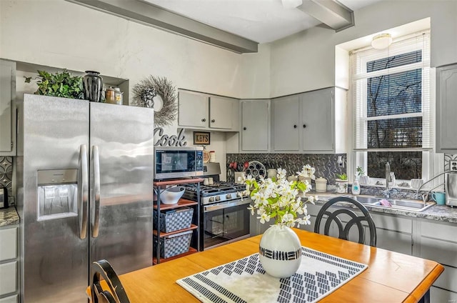 kitchen with beam ceiling, gray cabinets, light countertops, backsplash, and appliances with stainless steel finishes