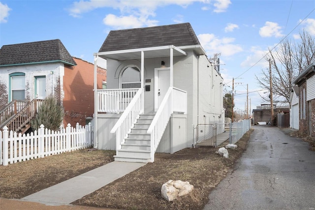 view of front facade featuring mansard roof, fence, covered porch, and a shingled roof