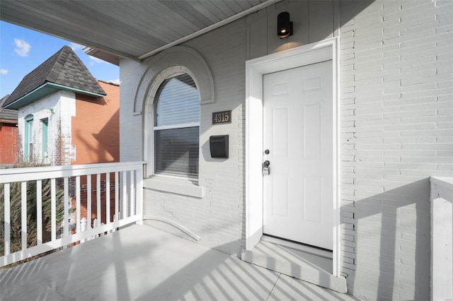 view of exterior entry with brick siding and a shingled roof