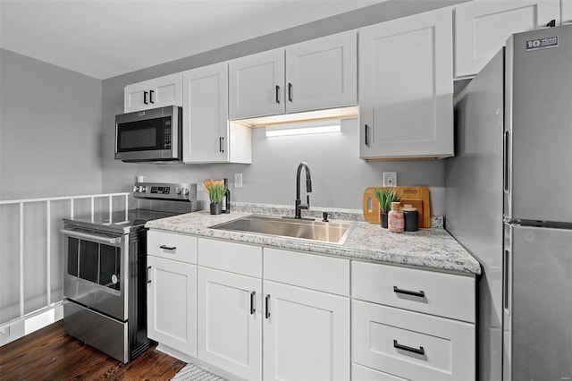 kitchen featuring light stone countertops, dark wood finished floors, a sink, white cabinets, and appliances with stainless steel finishes