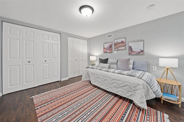 bedroom featuring visible vents, two closets, baseboards, and wood finished floors