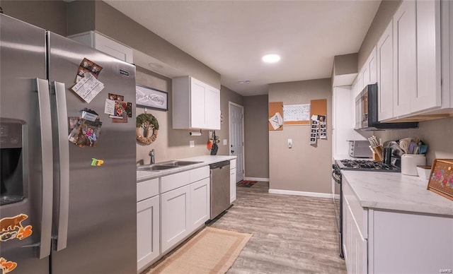 kitchen with light wood finished floors, stainless steel appliances, white cabinetry, a sink, and baseboards