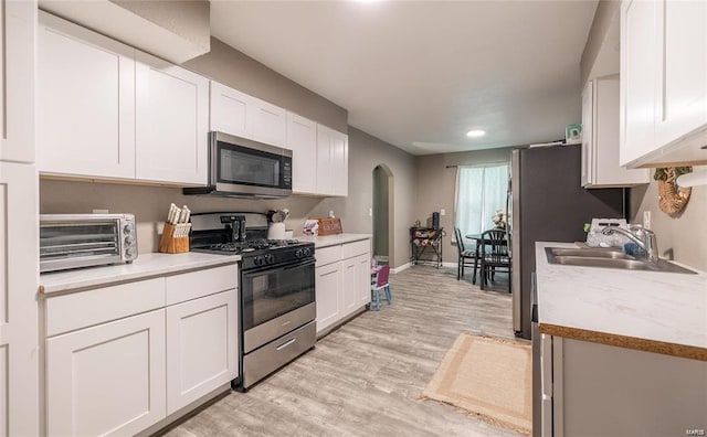 kitchen with a toaster, a sink, white cabinetry, light countertops, and appliances with stainless steel finishes