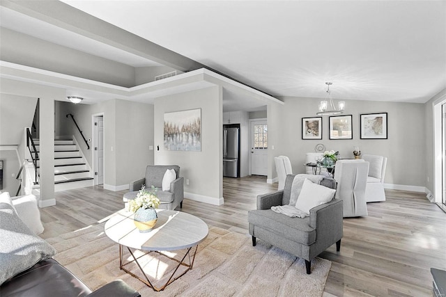 living room with light wood finished floors, vaulted ceiling, a chandelier, baseboards, and stairs