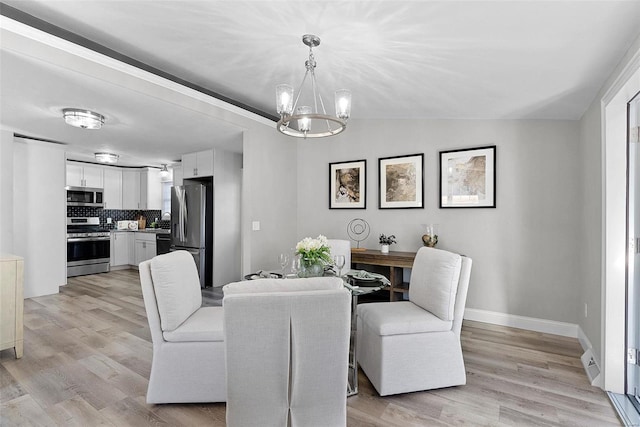 dining space with light wood-type flooring, an inviting chandelier, baseboards, and lofted ceiling