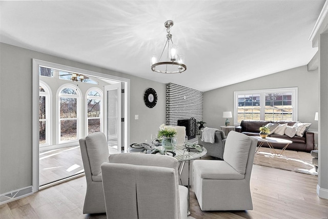 dining room with lofted ceiling, wood finished floors, a large fireplace, and an inviting chandelier