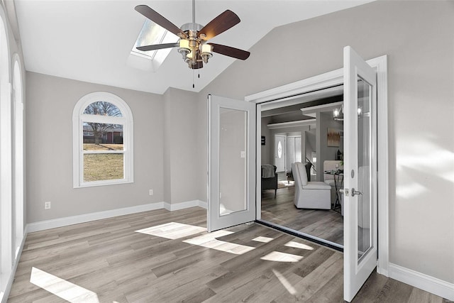 interior space featuring baseboards, a ceiling fan, lofted ceiling with skylight, french doors, and light wood-type flooring