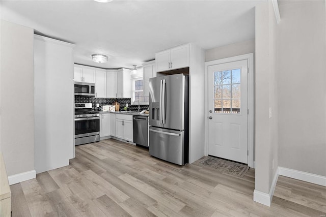 kitchen featuring decorative backsplash, appliances with stainless steel finishes, light wood-type flooring, white cabinetry, and a sink