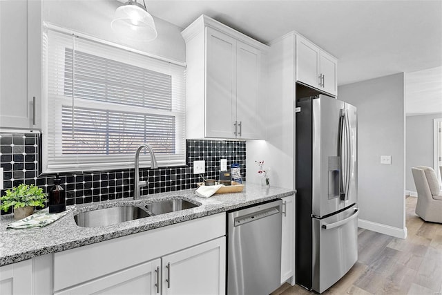 kitchen with appliances with stainless steel finishes, light wood-type flooring, a sink, and white cabinets