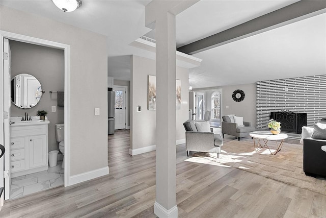 living area with vaulted ceiling with beams, a fireplace, baseboards, and wood finished floors