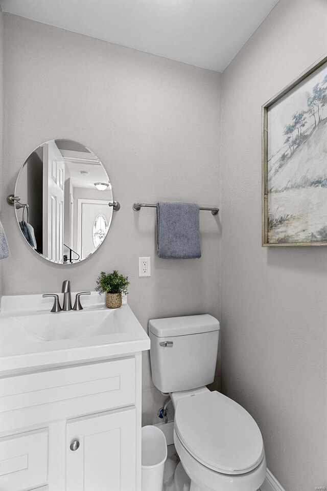 half bathroom featuring toilet, baseboards, and vanity